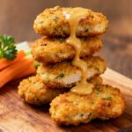 Air fryer paleo chicken nuggets with a crispy golden coating, juicy tender chicken inside, creamy dipping sauce, fresh parsley, and carrot and celery sticks, served as a healthy grain free meal.