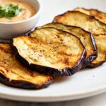 Air fryer eggplant chips with thin crispy roasted eggplant slices, lightly seasoned surfaces, caramelized edges, and a creamy dipping sauce, served as a healthy and satisfying snack.