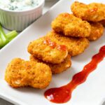 Air fryer buffalo chicken nuggets with a crispy golden coating, juicy tender chicken, spicy buffalo sauce, celery sticks, and dipping sauce, served as a flavorful appetizer or game day snack.