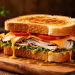 Air fryer turkey sandwich with sliced turkey, melted cheddar cheese, lettuce, tomato, and creamy sauce on toasted bread, served with fries and a lime wedge.