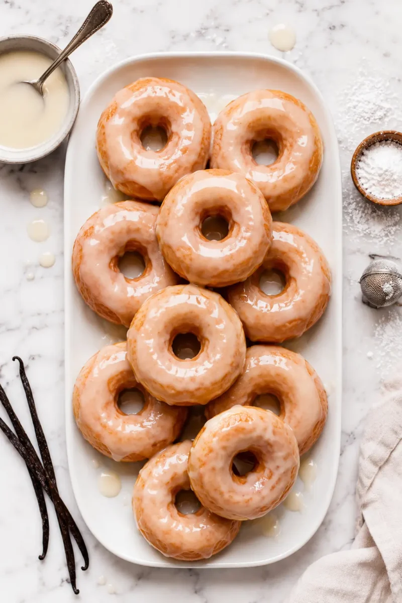 Air fryer glazed donuts topped with a sweet vanilla glaze and arranged on a serving platter with vanilla beans