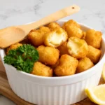 Frozen cheese curds cooked in the air fryer with a crispy golden breaded coating and gooey melted cheese center, served in a bowl with fresh parsley and lemon wedges.