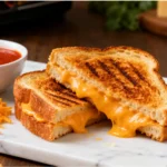 Air fryer grilled cheese sandwich with crispy golden toasted bread, gooey melted cheddar cheese, grill marks, and a rich buttery texture, served with tomato soup for a comforting meal.