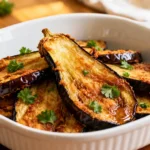Air fryer fried eggplant slices with golden caramelized surfaces, tender creamy centers, lightly crisp edges, and fresh parsley garnish, served as a simple and flavorful vegetable side dish.