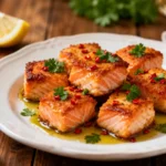 Air fryer Cajun salmon bites with crispy seasoned salmon cubes, bold Cajun spices, fresh parsley, red pepper flakes, and lemon wedges, served as a spicy high protein appetizer or dinner.