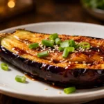 Air fryer Chinese eggplant with tender roasted eggplant halves, a glossy savory sauce, toasted sesame seeds, sliced green onions, and caramelized edges, served as a flavorful Asian inspired side dish.