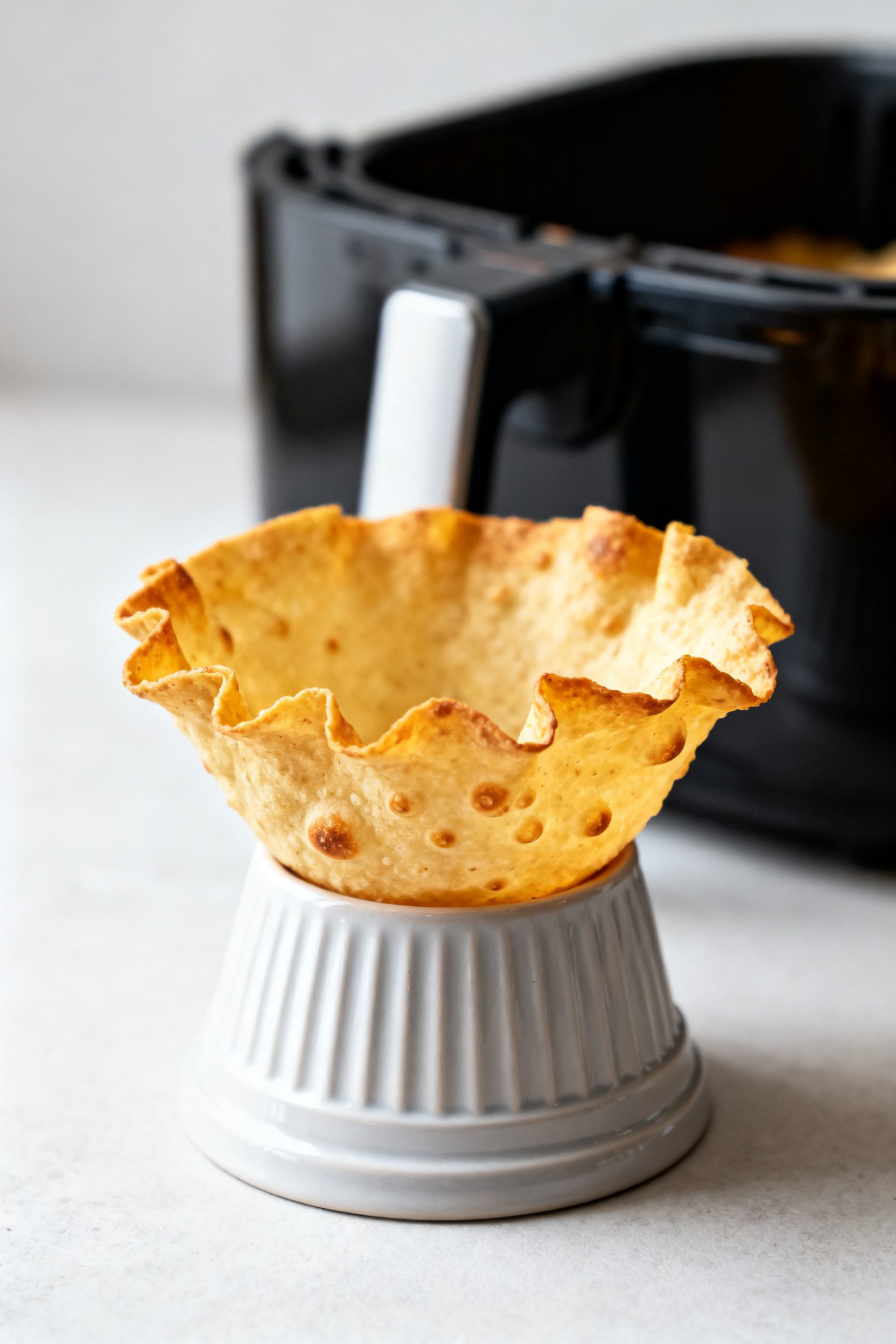 Close-up detail: Golden, air-fried tortilla bowl just out of the basket, crisp ruffled edges and tin