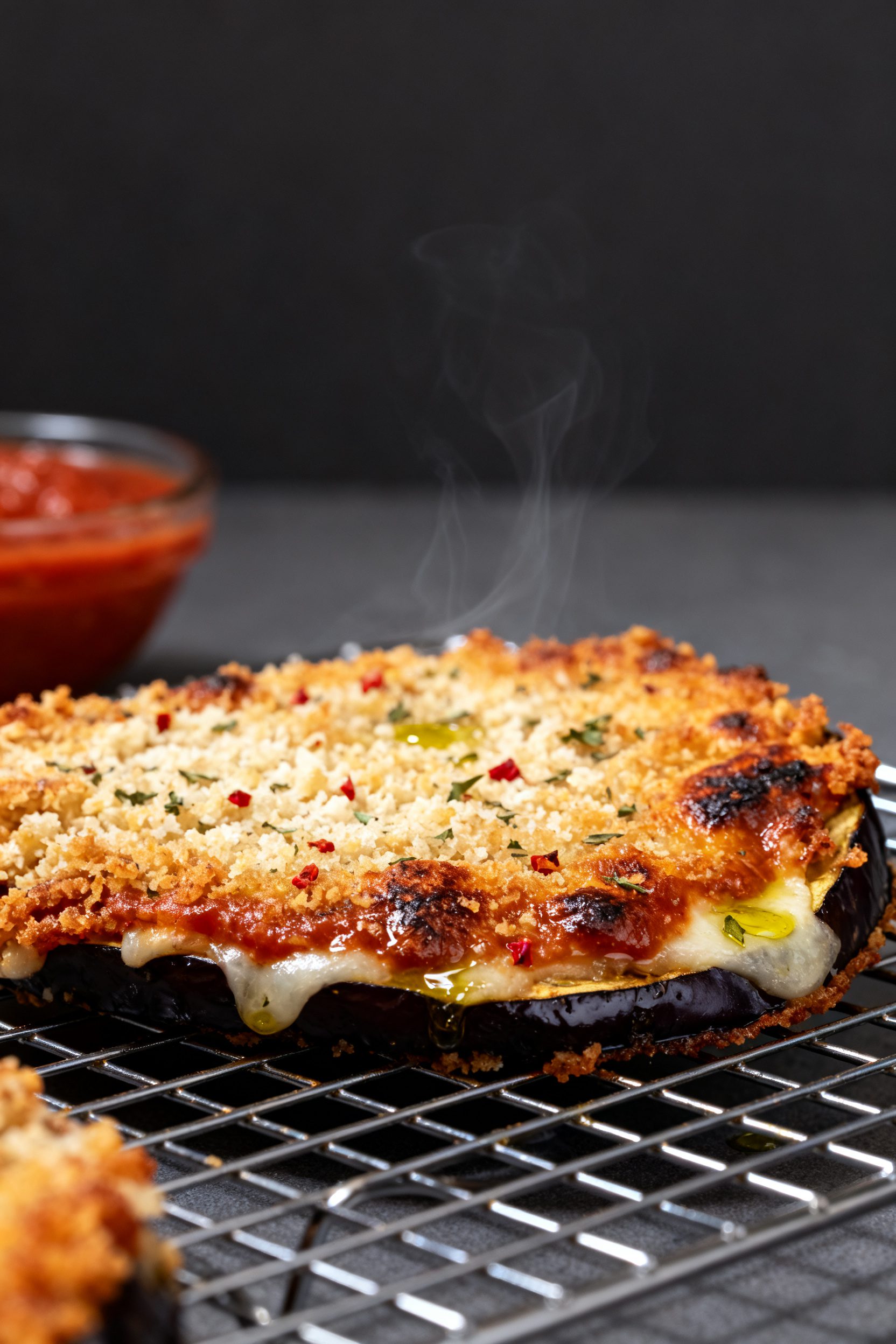 Close-up detail shot: A just-air-fried eggplant parmesan slice on a wire rack, coating blistered and