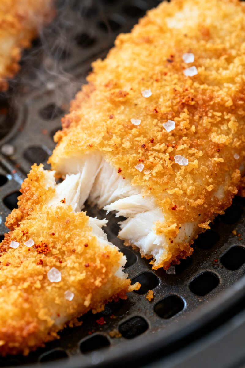 Close-up detail shot: Golden, panko-crusted air-fryer cod just out of the basket, coating visibly sh