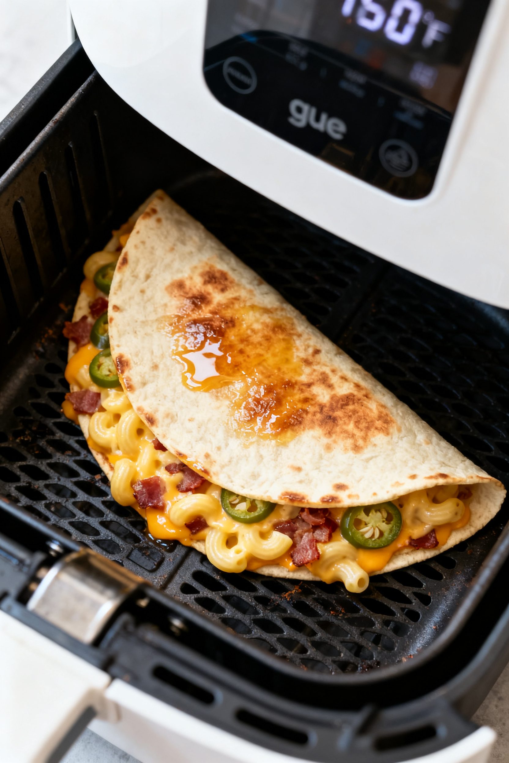 Cooking process: Overhead shot of a half-moon quesadilla inside an open air fryer basket mid-cook, b