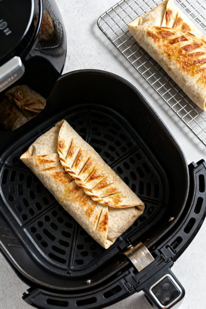 Cooking process: Overhead shot of a sealed crunch wrap in an air fryer basket, seam side down, mid-c