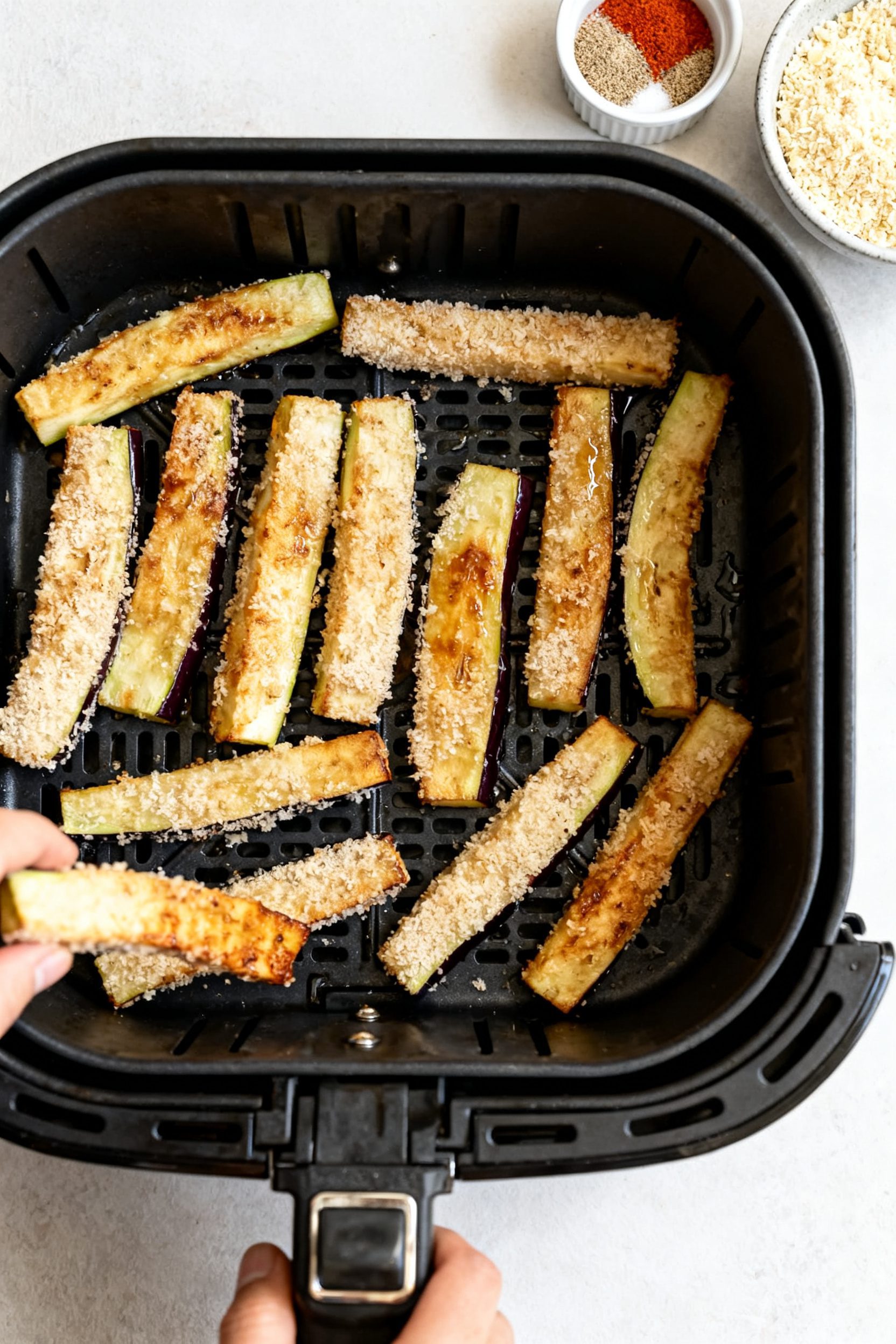 Cooking process: Overhead shot of a single-layer batch of breaded eggplant sticks arranged with spac