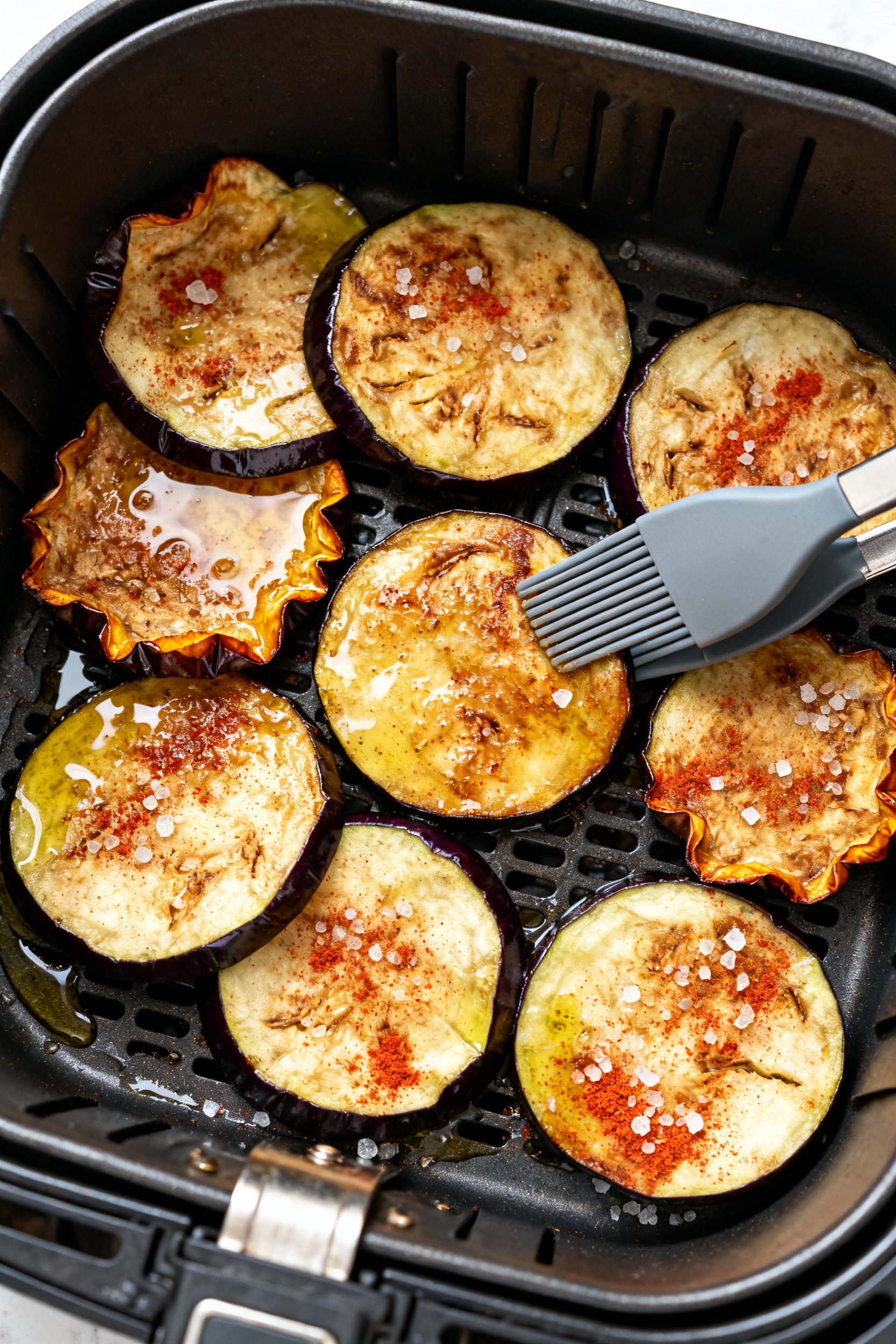 Cooking process: Overhead shot of a single layer of seasoned eggplant rounds arranged in an air frye