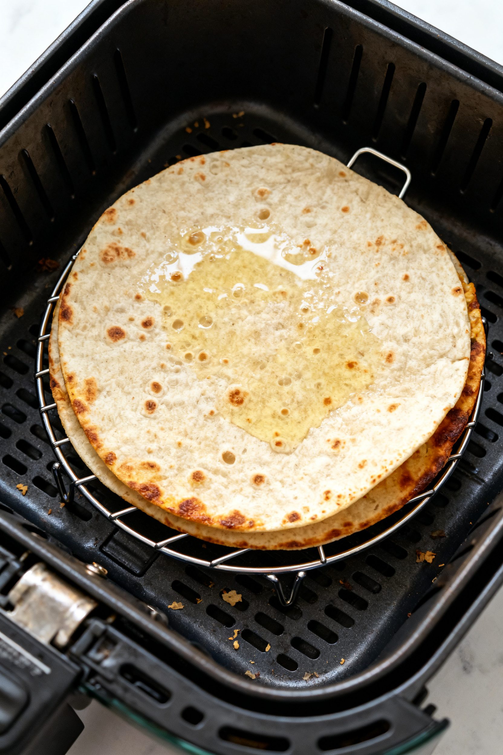 Cooking process: Overhead shot of a two-tortilla quesadilla in the air fryer basket at 375°F, top t