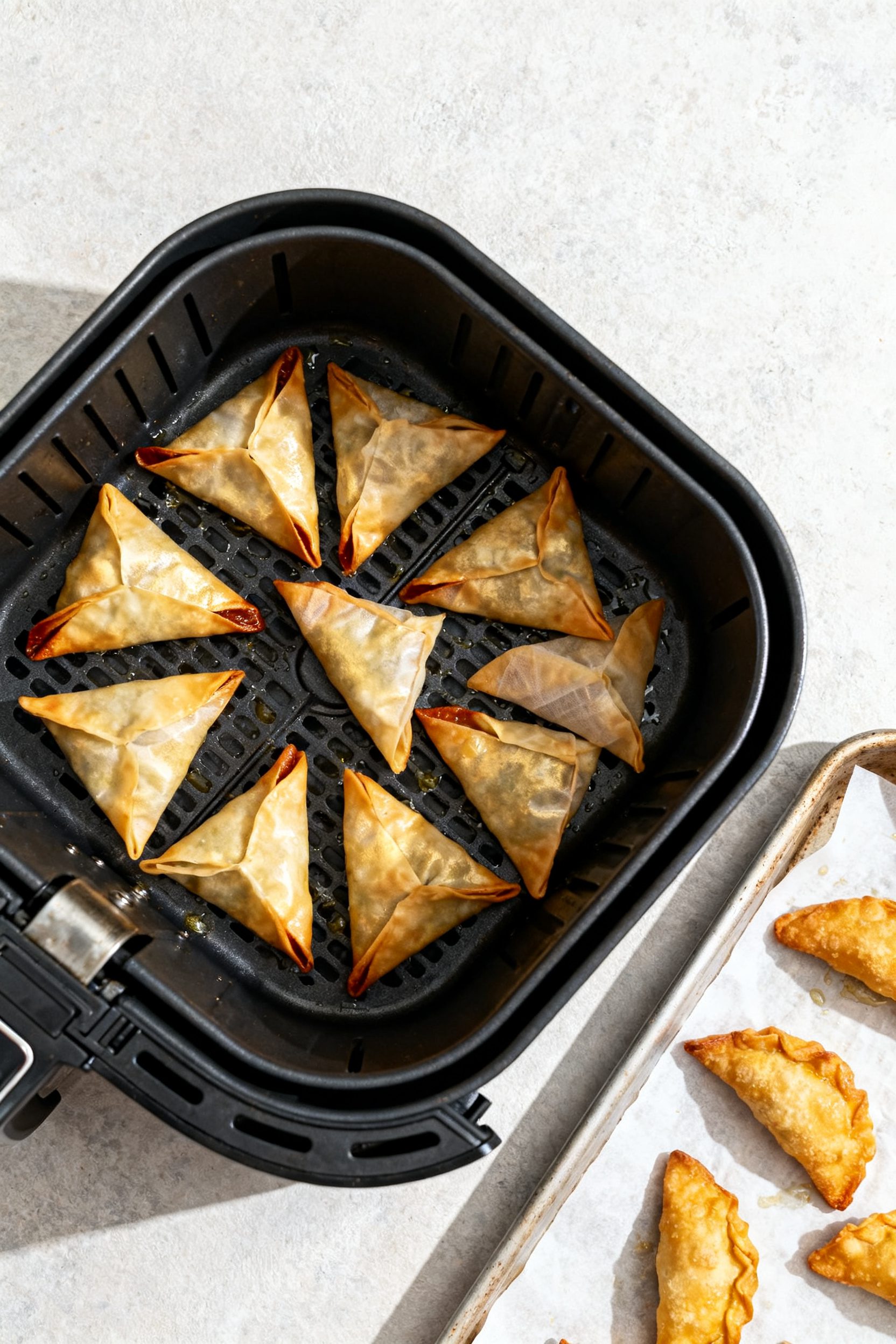 Cooking process: Overhead shot of an air fryer basket with a single-layer arrangement of sealed tria
