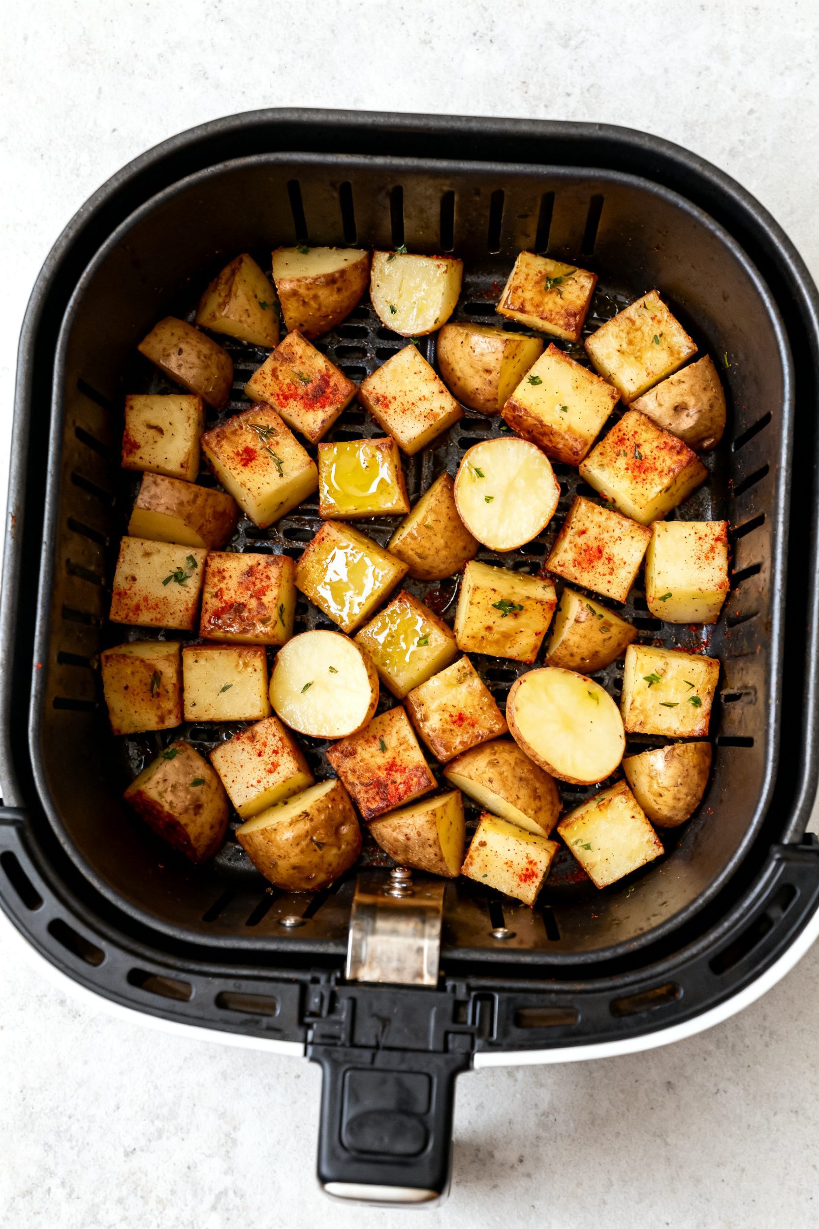Cooking process: Overhead shot of an open air fryer basket at the halfway point, potatoes in a singl