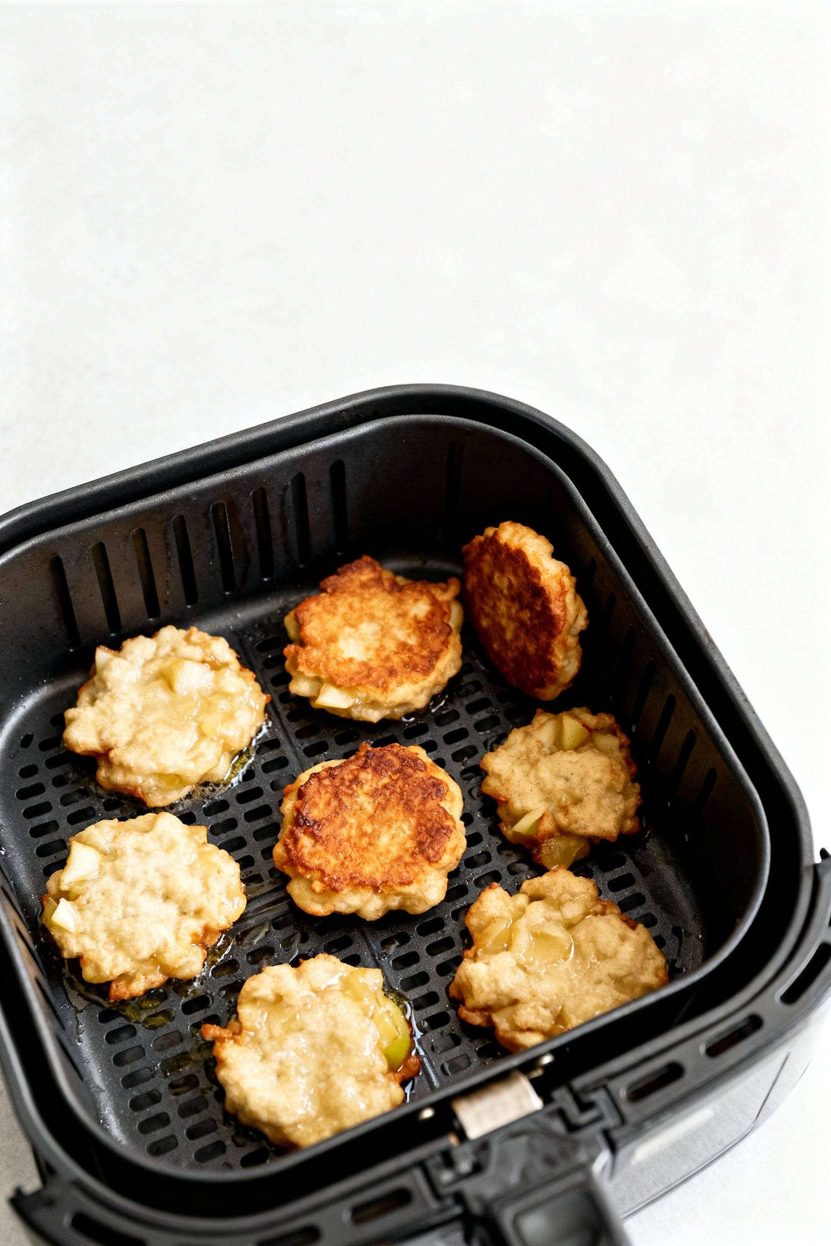 Cooking process: Overhead shot of apple fritter mounds mid-cook in an air fryer at 370°F—evenly s