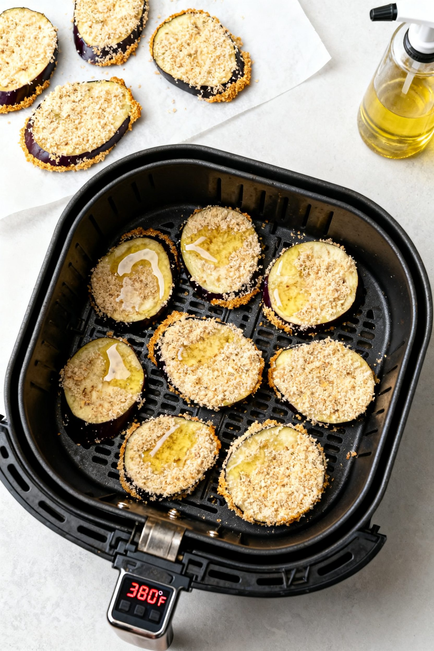 Cooking process: Overhead shot of coated eggplant slices arranged in a single layer inside a preheat