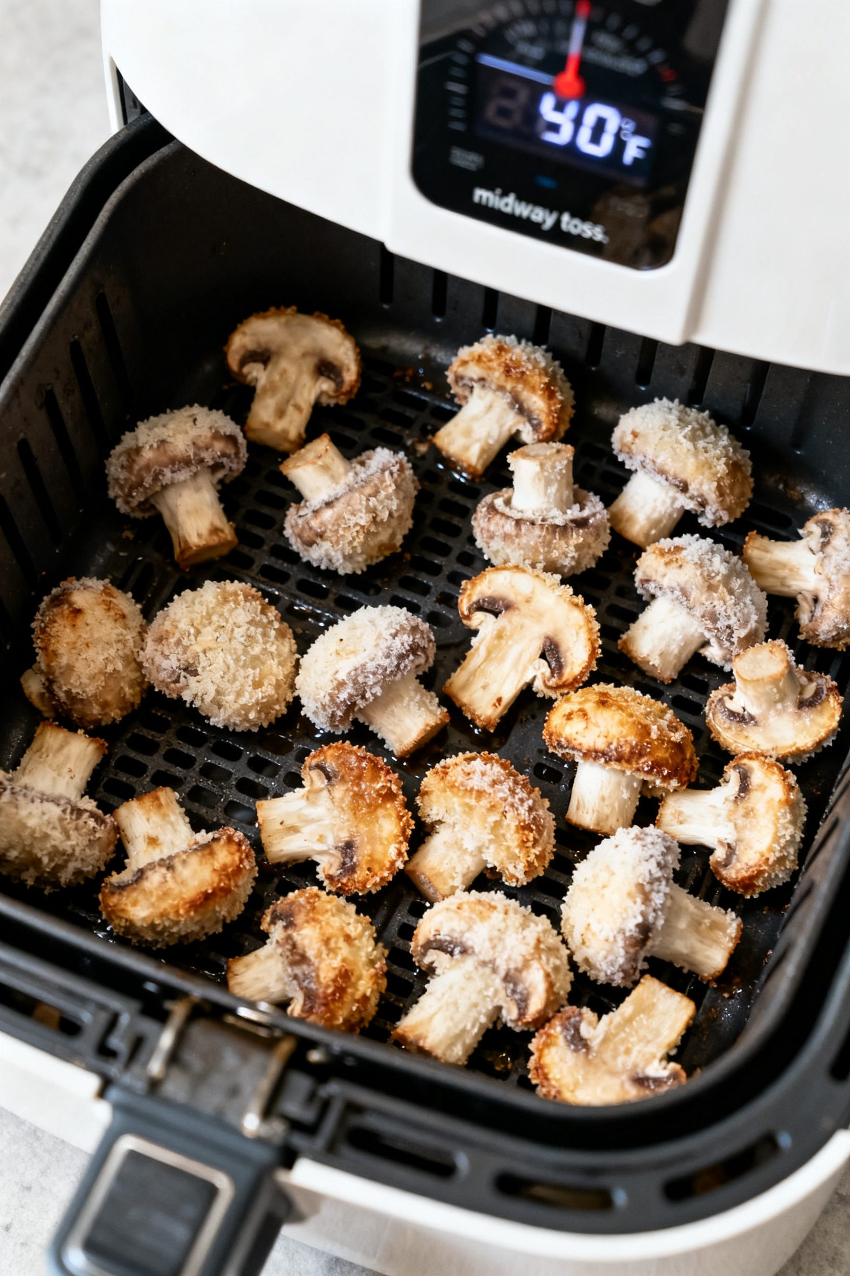 Cooking process: Overhead shot of frozen breaded mushrooms mid-cook in an open air fryer basket at 3