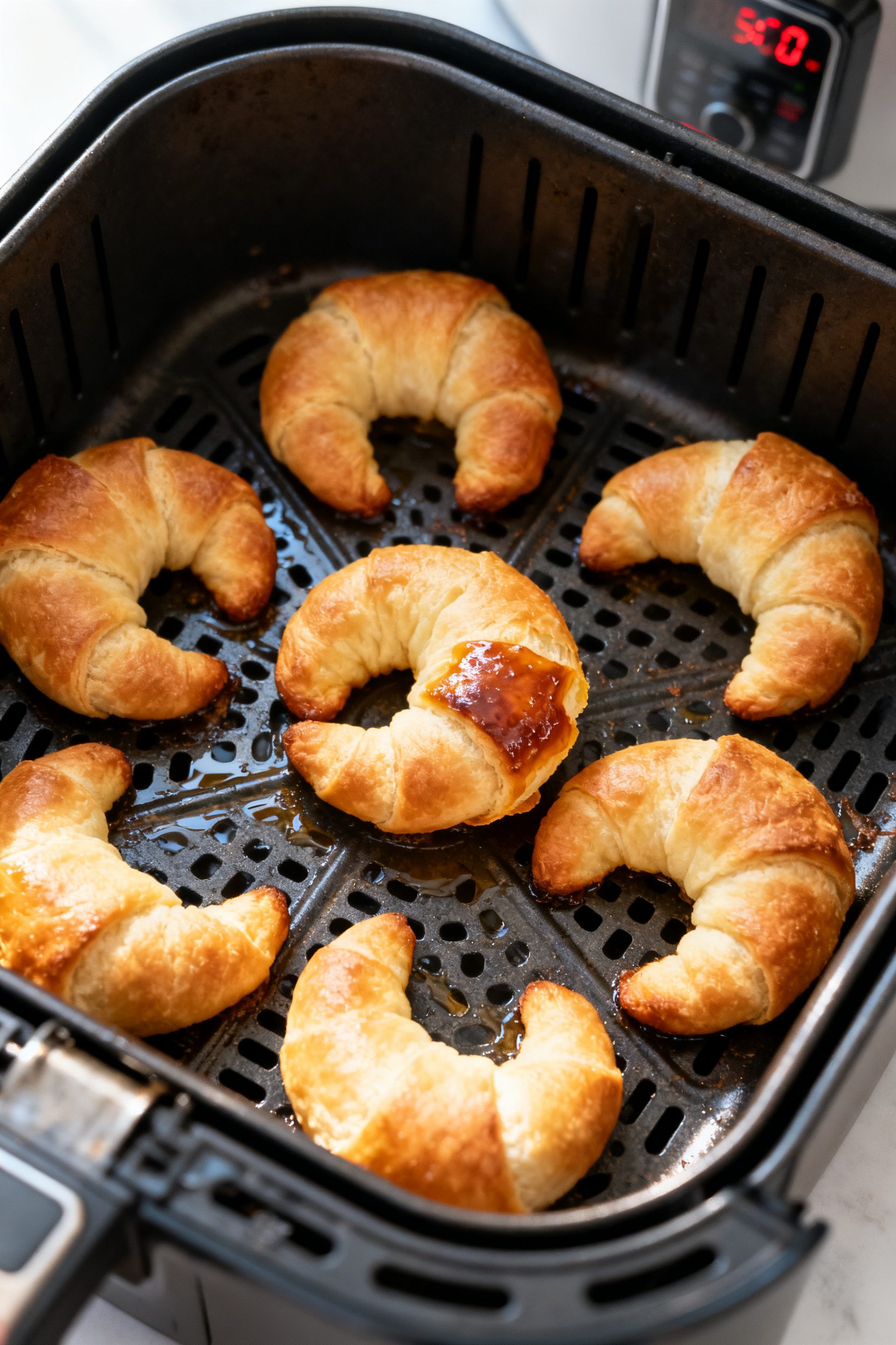 Cooking process: Overhead shot of golden crescent roll donuts mid-cook in an air fryer basket at 350