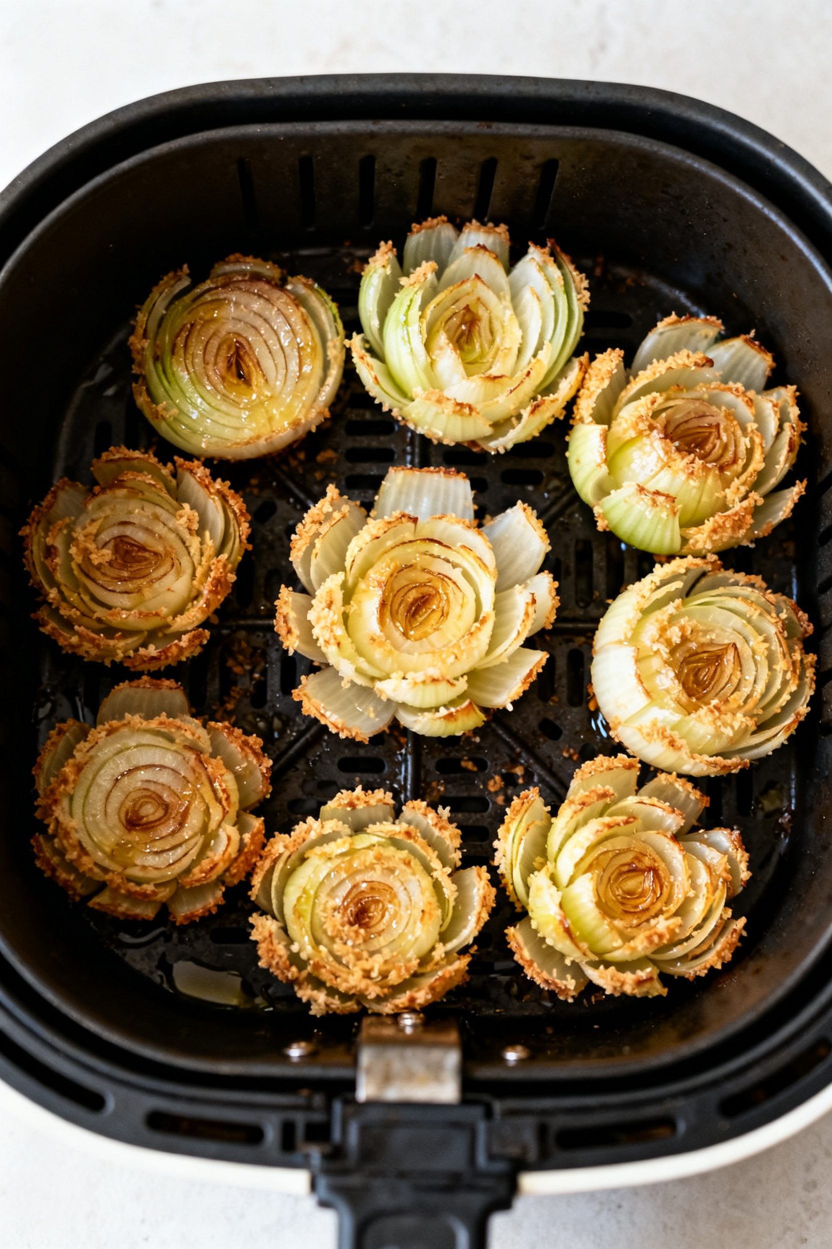 Cooking process: Overhead shot of multiple mini blooming onions arranged cut-side up in an air fryer