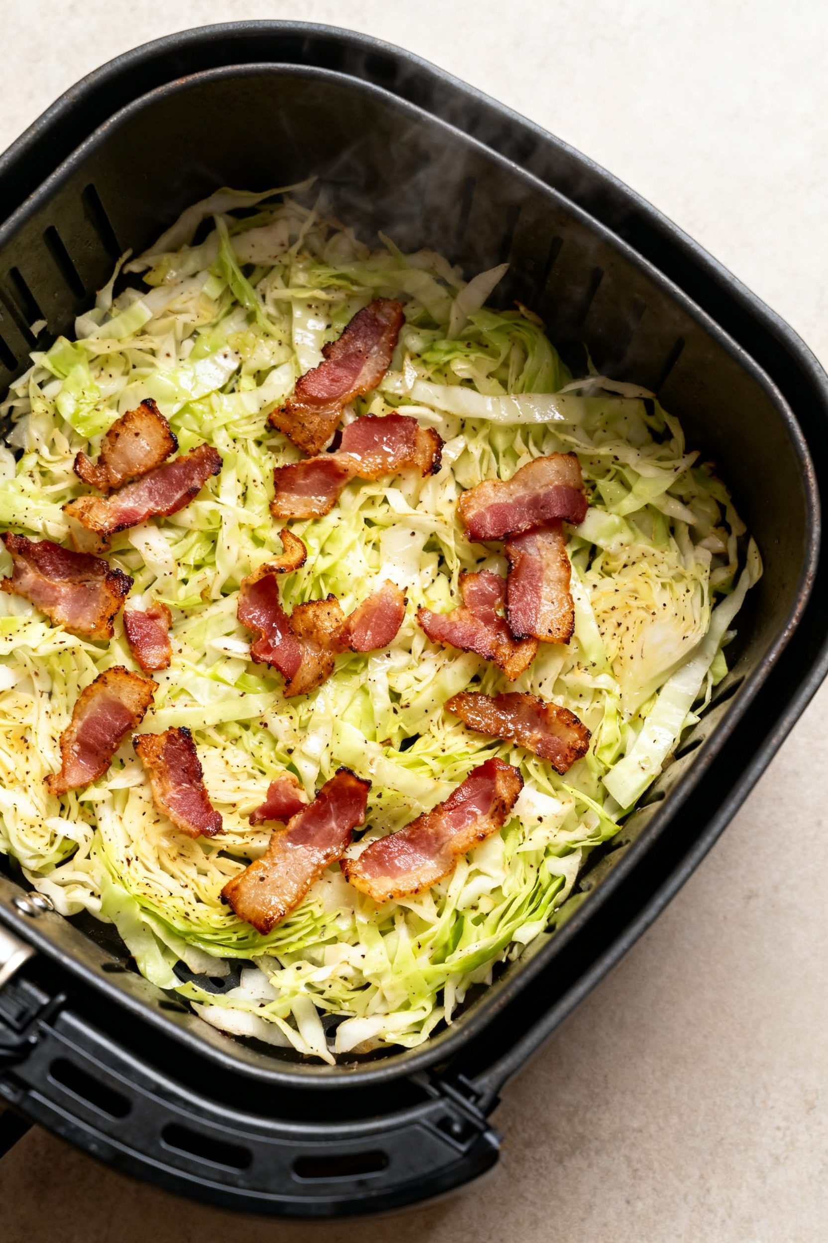 Cooking process: Overhead shot of seasoned cabbage shreds mid-cook in an air fryer basket at 375°F 