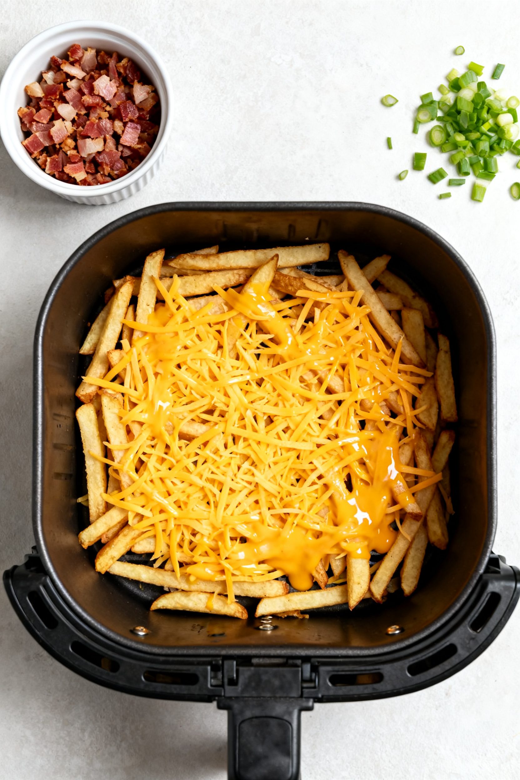 Cooking process shot: Overhead view inside the air fryer right after adding shredded cheddar (or che