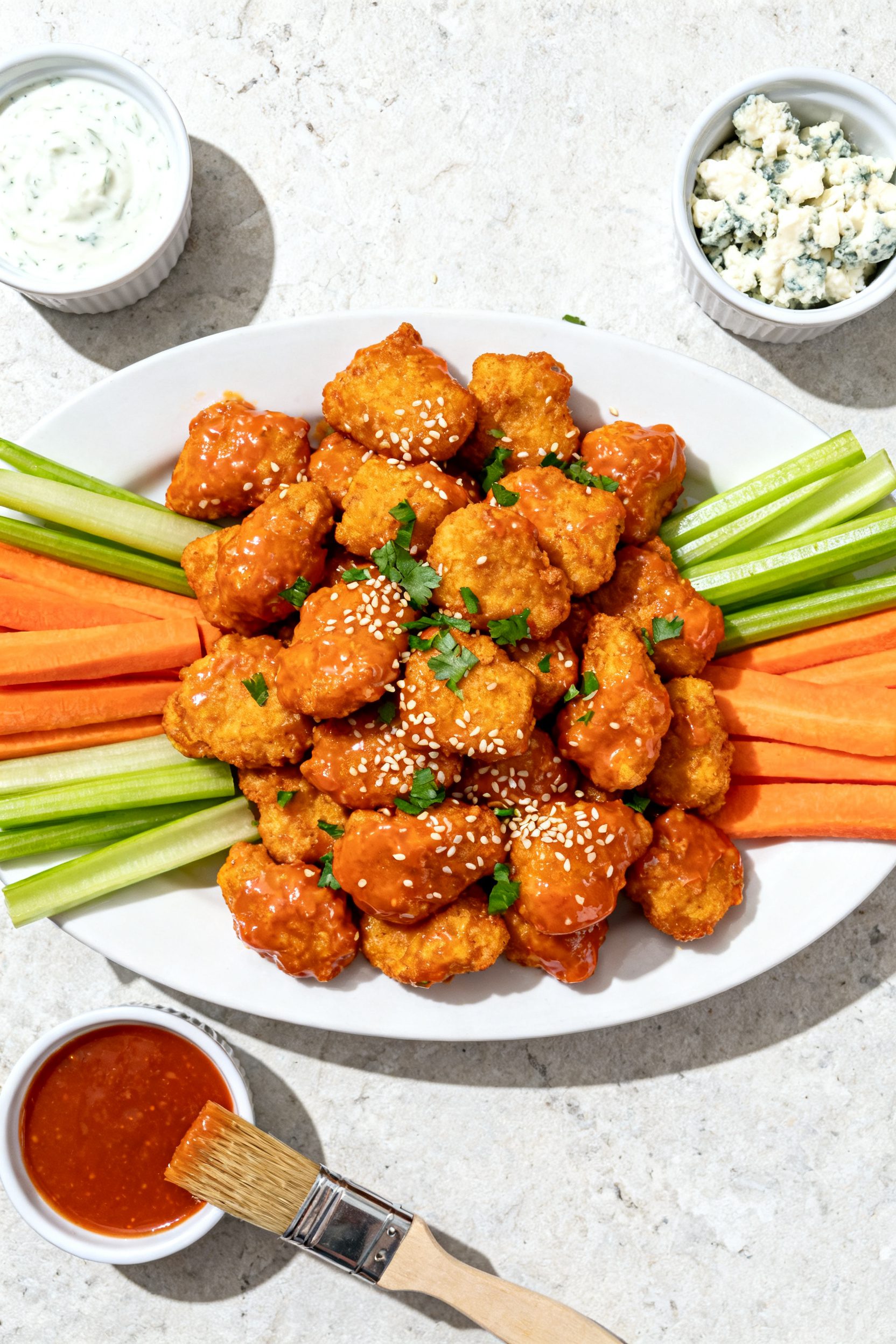 Overhead “tasty top view” of a game-day platter: a heaping pile of buffalo chicken nuggets cente