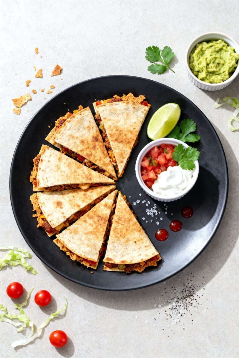 Air fryer beef quesadilla sliced into wedges and served with guacamole, salsa, sour cream, and lime