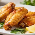 Air fryer low carb chicken wings with crispy golden skin, juicy tender meat, fresh rosemary, parsley, and lemon wedges, served as a flavorful keto friendly appetizer or dinner.
