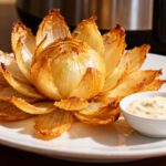 Air fryer homemade blooming onion with crispy golden onion petals, tender center, and a creamy dipping sauce, served as a lighter version of the classic restaurant appetizer.