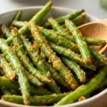 Air fryer keto green beans with tender crisp green beans coated in a savory garlic and parmesan seasoning, served as a quick low carb side dish with a wooden spoon.
