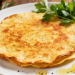 Air fryer low carb tortilla with a crispy golden browned surface, thin crunchy texture, fresh parsley, cherry tomatoes, and a drizzle of olive oil, served as a versatile keto friendly base for wraps or pizzas.