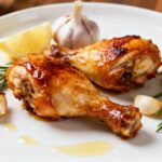 Air fryer keto chicken legs with crispy golden skin, juicy tender meat, fresh rosemary, roasted garlic, and a lemon wedge, served as a flavorful low carb dinner.