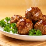 Frozen meatballs cooked in the air fryer with browned crispy exteriors, juicy tender centers, fresh parsley garnish, and lemon wedges, served as a quick and easy appetizer or dinner.