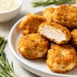 Air fryer keto chicken bites with a crispy golden low carb coating, juicy tender chicken inside, fresh rosemary, lemon wedge, and creamy dipping sauce, served as a high protein keto friendly meal.