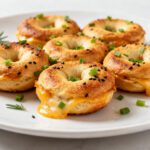 Air fryer keto bagel bites with golden browned mini bagels, gooey melted cheddar cheese, sliced green onions, black sesame seeds, and fresh herbs, served as a low carb breakfast or snack.