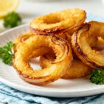 Air fryer easy onion rings with a crispy golden coating, tender sweet onion centers, fresh parsley garnish, and lemon wedges, served as a crunchy appetizer or flavorful side dish.