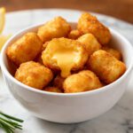Air fryer keto cheese curds with a crispy golden low carb coating, gooey melted cheese centers, fresh rosemary, and lemon wedges, served as a crunchy keto friendly appetizer or snack.
