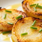 Air fryer grilled onions with sweet caramelized onion halves, lightly charred edges, fresh chives, and a drizzle of olive oil, served as an easy and flavorful vegetable side dish.