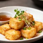 Air fryer agedashi tofu with crispy golden tofu cubes, savory dipping broth, fresh microgreens, sliced green onions, and bonito flakes, served as a light Japanese inspired appetizer.
