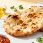 Air fryer naan bread with a soft chewy texture, charred golden bubbles, olive oil, and fresh cilantro, served as a warm homemade flatbread with dipping sauces.
