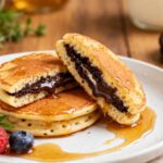 Air fryer Oreos with pancake batter featuring golden fluffy pancakes filled with chocolate sandwich cookies, warm melted chocolate cream, maple syrup, and fresh berries, served as a fun homemade dessert.