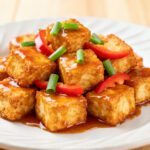 Air fryer sweet and sour tofu with crispy golden tofu cubes, glossy sweet and sour sauce, red bell peppers, and fresh green onions, served as a colorful vegetarian weeknight dinner.