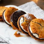 Air fryer deep fried Oreos with crispy golden batter, chocolate sandwich cookies, sweet cream filling, powdered sugar, and caramel drizzle, served as a fun fair inspired dessert.