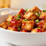 Air fryer General Tso tofu with crispy golden tofu cubes coated in a glossy sweet and spicy sauce, topped with sesame seeds and green onions, served as a flavorful vegetarian weeknight dinner.