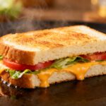Air fryer sandwich bread with soft toasted white bread, melted cheddar cheese, fresh lettuce, sliced tomatoes, and steam rising, served as a quick homemade sandwich.