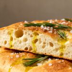 Air fryer focaccia bread with a crispy golden crust, chewy airy crumb, rosemary sprigs, flaky sea salt, and olive oil, served as a rustic homemade Italian bread.