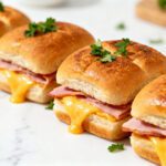 Air fryer ham and cheese sliders with soft golden slider buns, savory sliced ham, gooey melted cheddar cheese, buttery tops, and fresh parsley, served as an easy party appetizer.