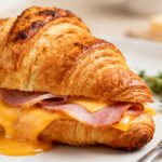 Air fryer ham and cheese croissant with flaky buttery croissant, savory sliced ham, gooey melted cheddar cheese, and fresh rosemary, served as a warm breakfast or brunch sandwich.